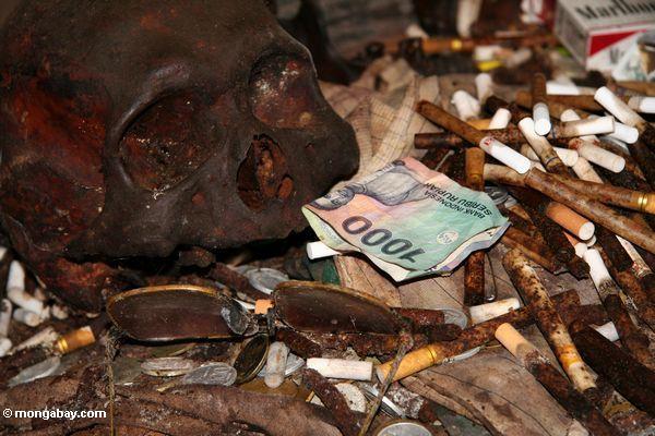 Rupiahanmerkung unter Zigaretten und Münzen am ernsten Aufstellungsort in der Höhle bei Londa
