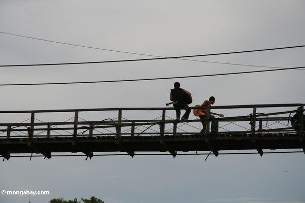 男性は川の橋の上でギターを弾く