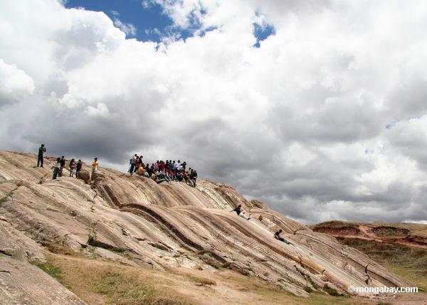 Kinder, die hinunter glatten Felsen bei Sacsayhuaman schieben